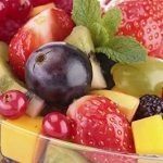 Primer plano bol de cristal con fresas, uvas negras, mango, piña