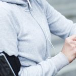mujer sudadera gris portamóvil brazo derecho pulsera actividad brazo izquierdo cable de auriculares