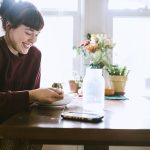 mujer sonriendo sentada con los brazos apoyados en la mesa comiendo de un plato