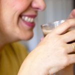 primer plano perfil mujer sonrisa labios rojos, manos sujetan taza de café